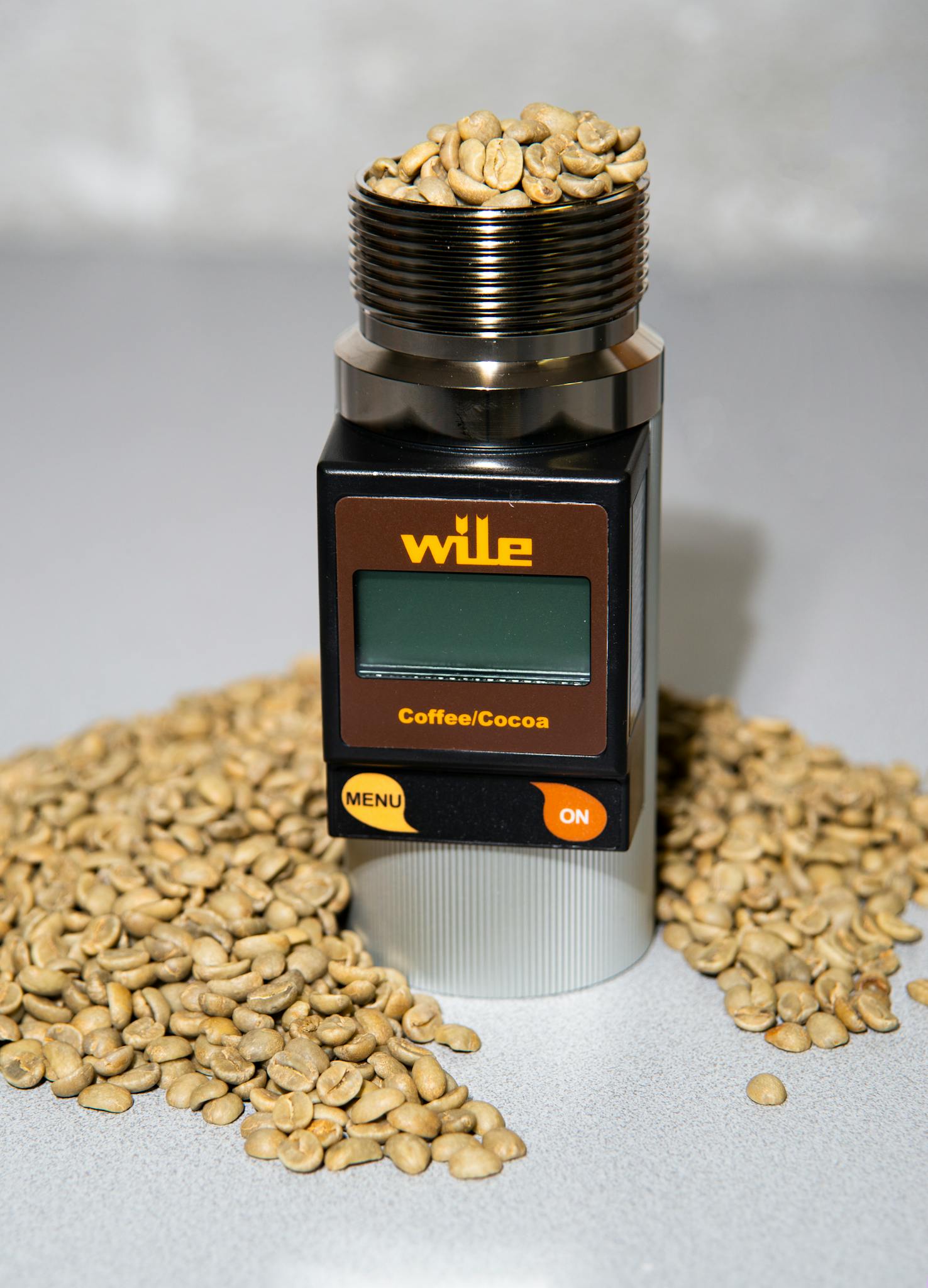 Detailed view of a coffee moisture tester surrounded by scattered coffee beans on a surface.